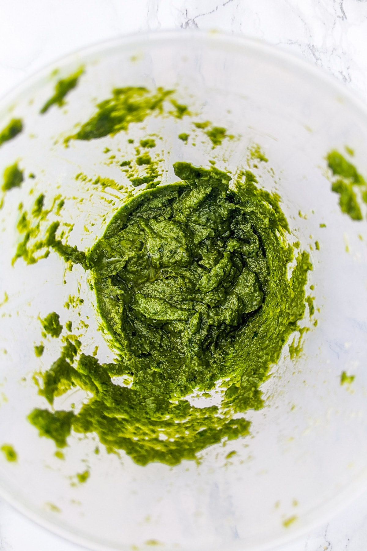 Close look of mixed fresh basil pesto in a plastic rounded container.