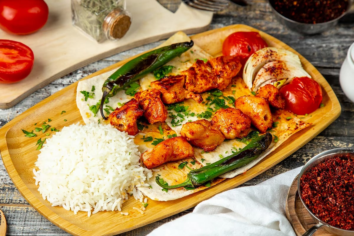 A close look at Arabic chicken dishes with rice, and roasted vegetables on a wooden plate.