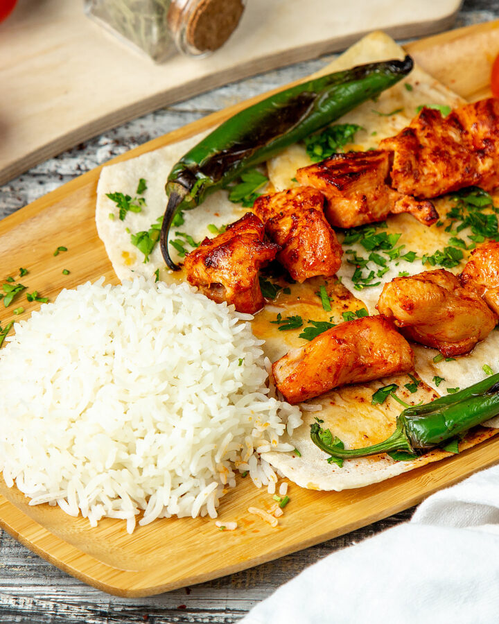 A close look at Arabic chicken dishes with rice, and roasted vegetables on a wooden plate.