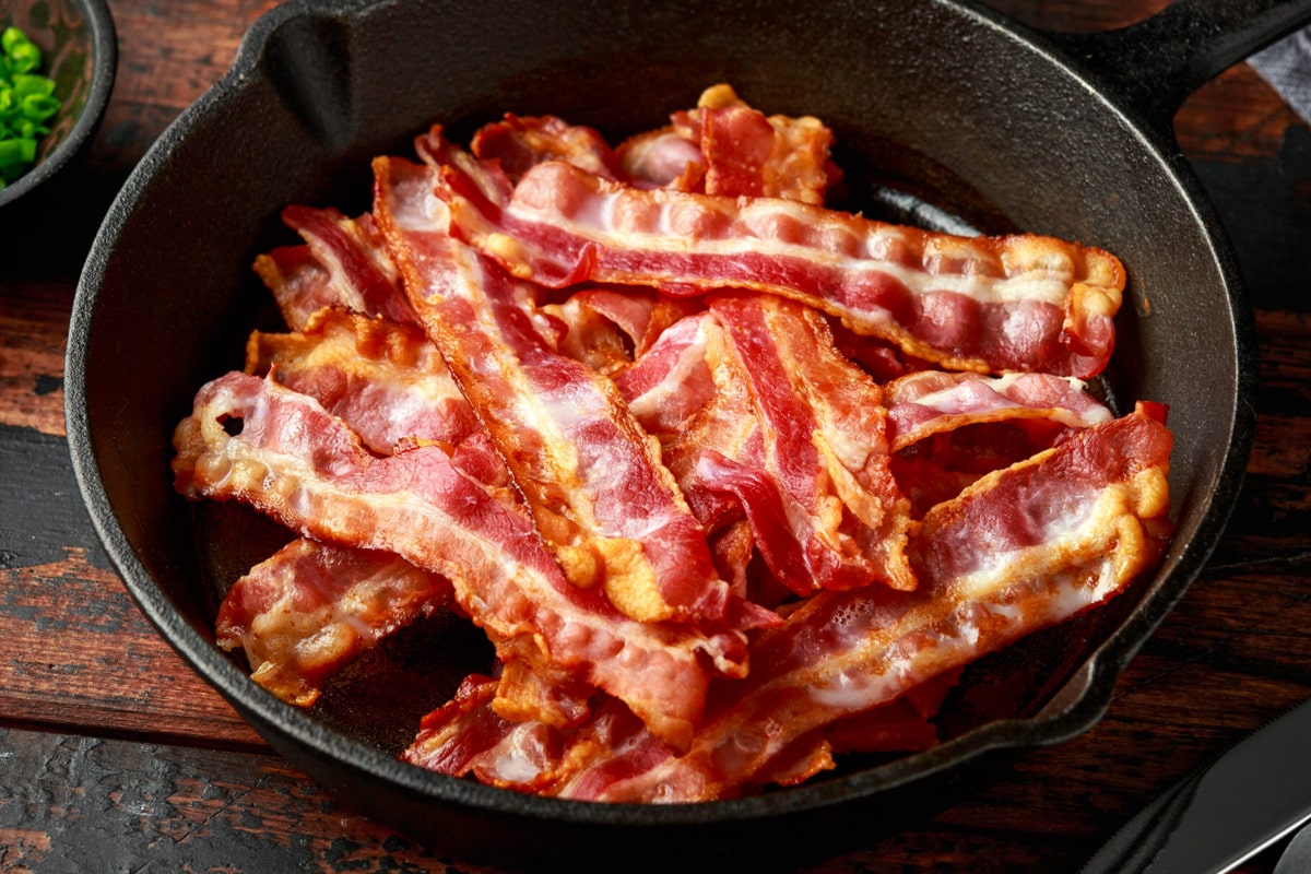Close view of an iron skillet with fried bacon slices.