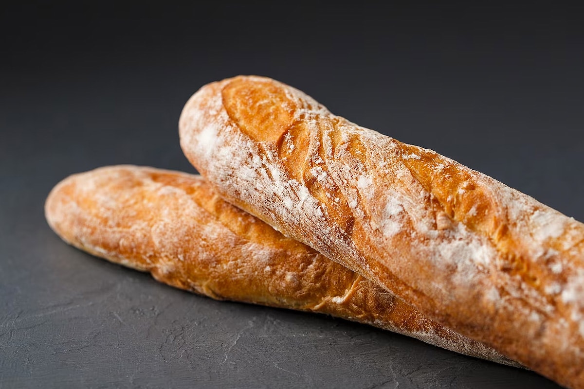 Close look of two French baguettes on a dark grey background.