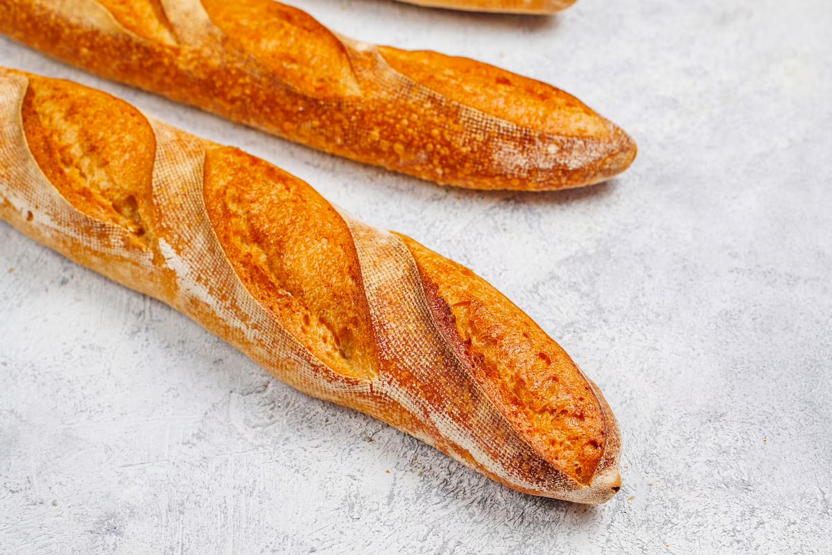 Two fresh French baguettes on a light dark table.