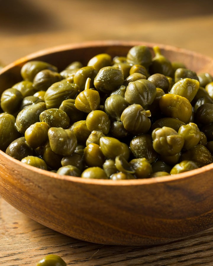 Close look of a wooden bowl with salted capers on a wooden table.