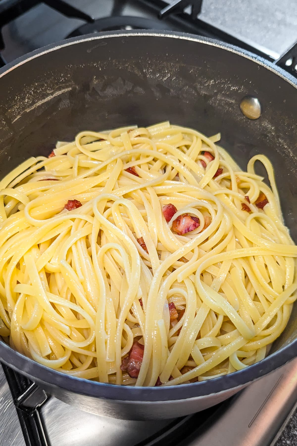 Boiled spaghetti mixed with fried bacon pieces.