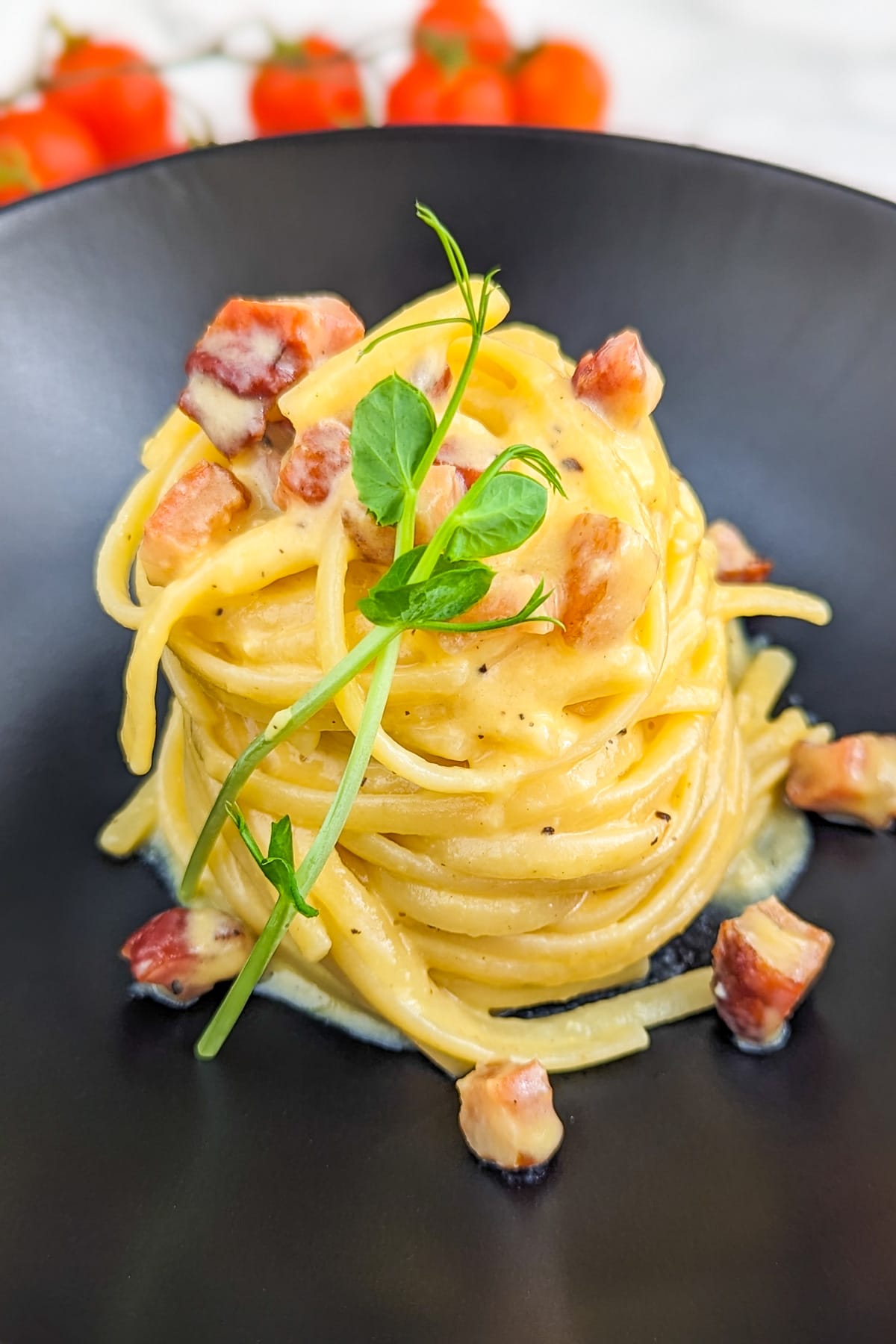 Elegant carbonara pasta with bacon arranged on a black plate.