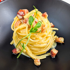 Elegant carbonara pasta with bacon arranged on a black plate.