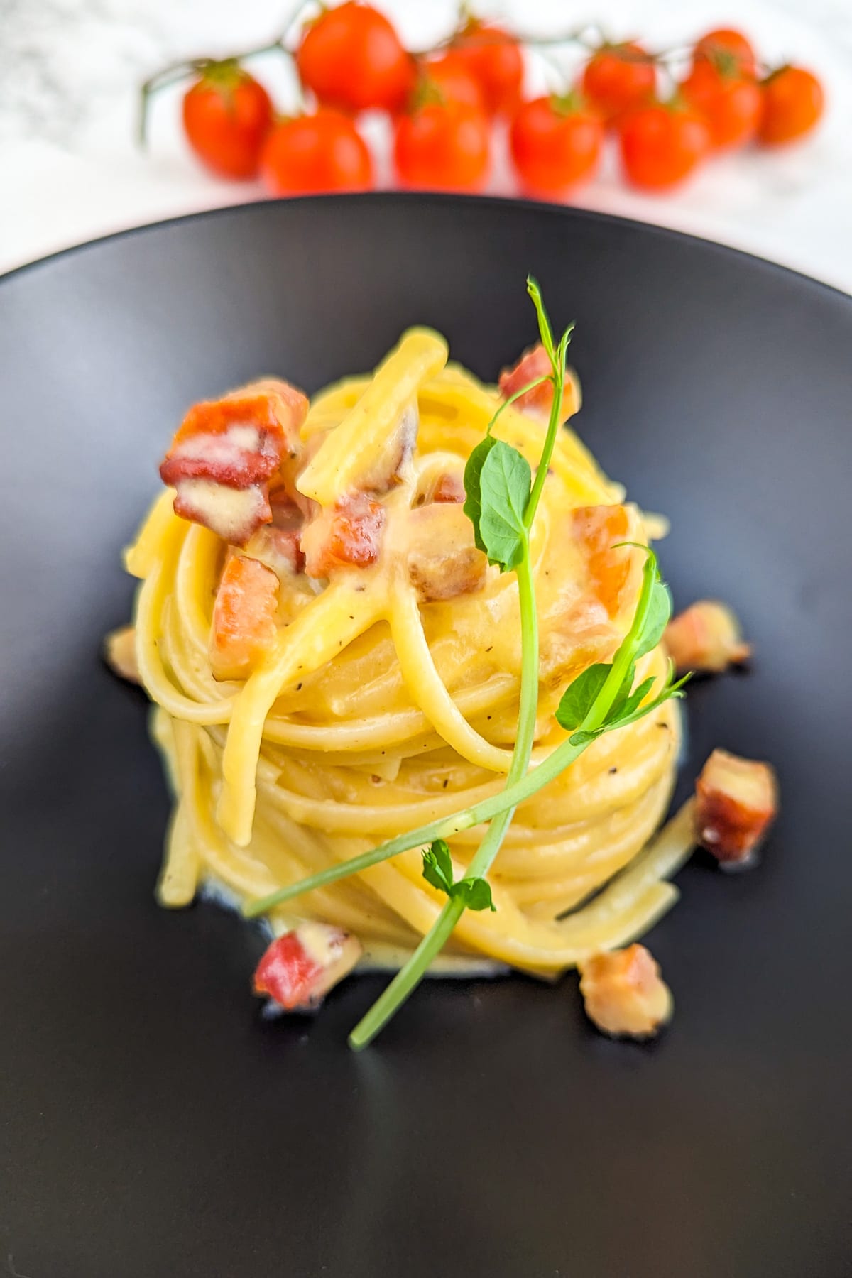 Elegant plating of carbonara pasta with bacon served on a black plate.