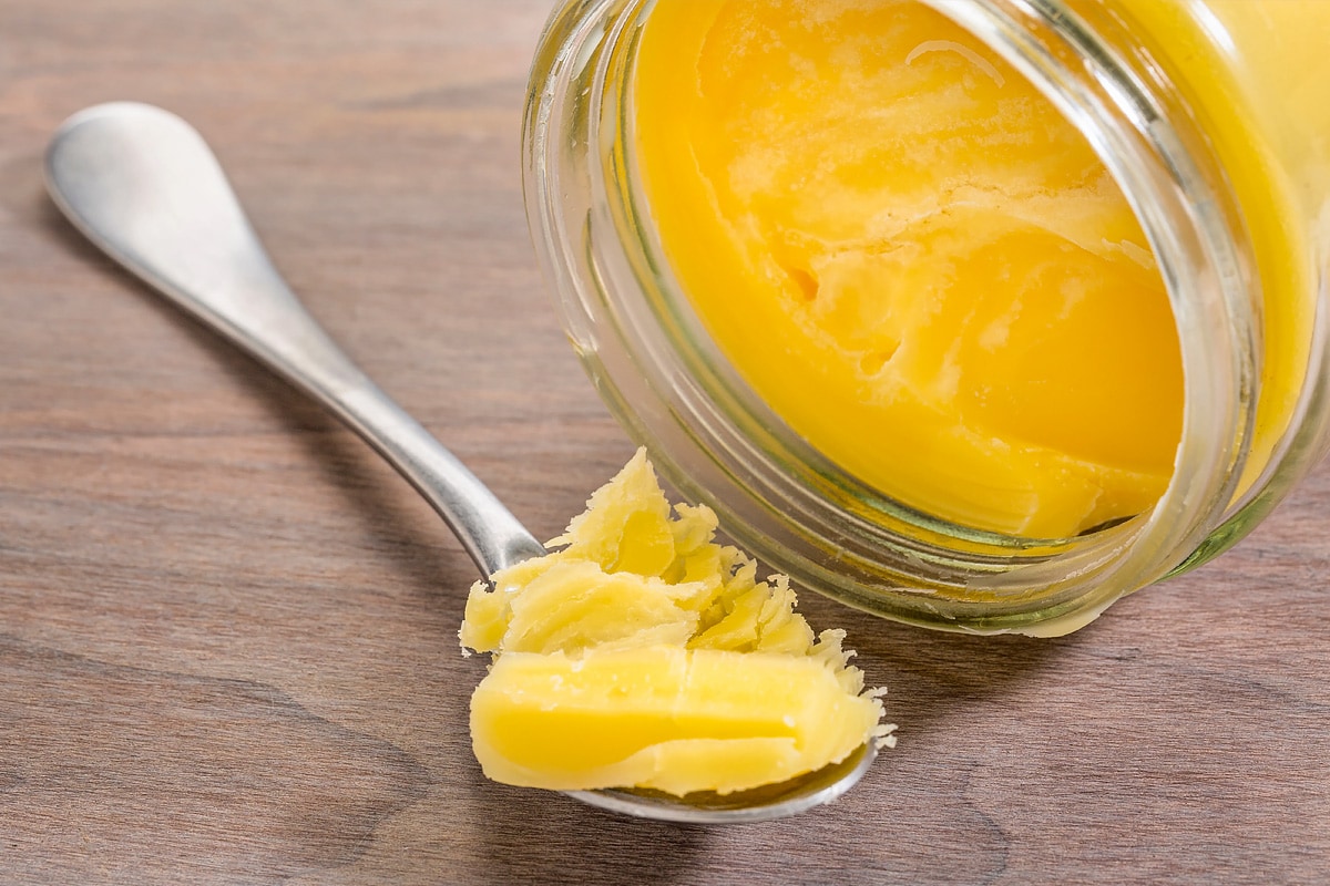 Metal spoon with ghee butter near a transparent jar.