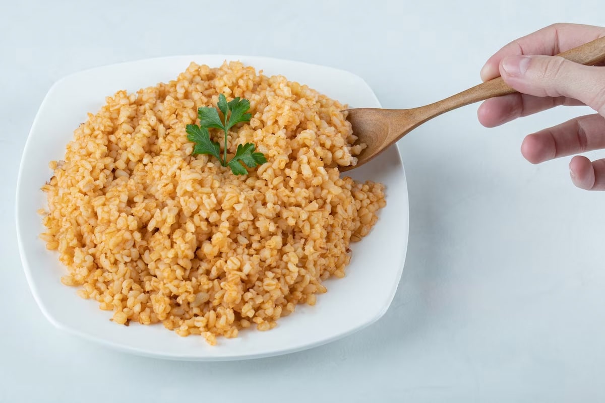 Man hand holding a wooden spoon with cooked bulgur.