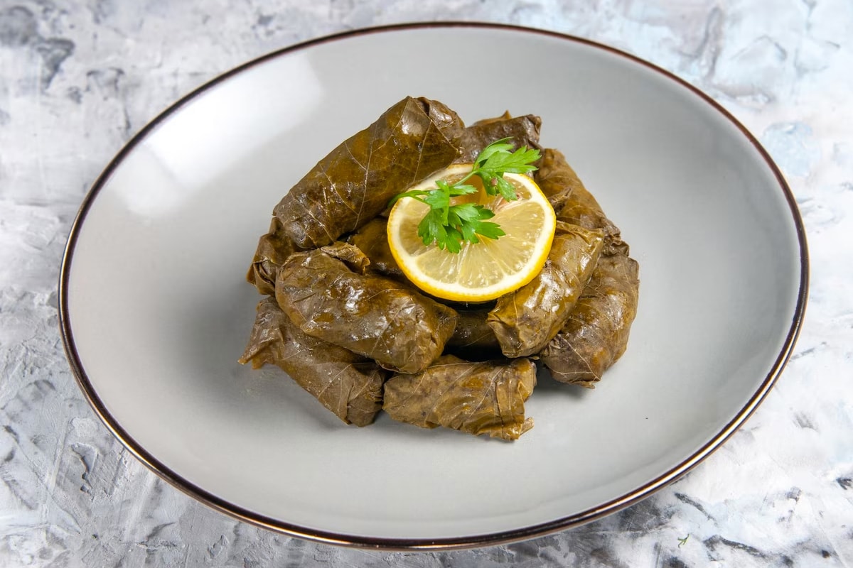 Gray plate with dolmas, a lemon slice, and parsley on a gray table.