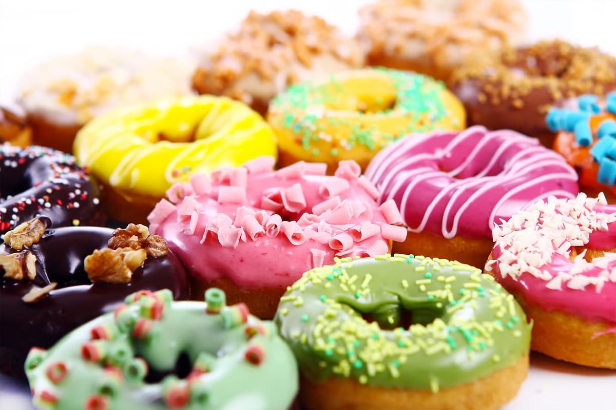 Close look of multiple donuts of different colors sitting on a white table.