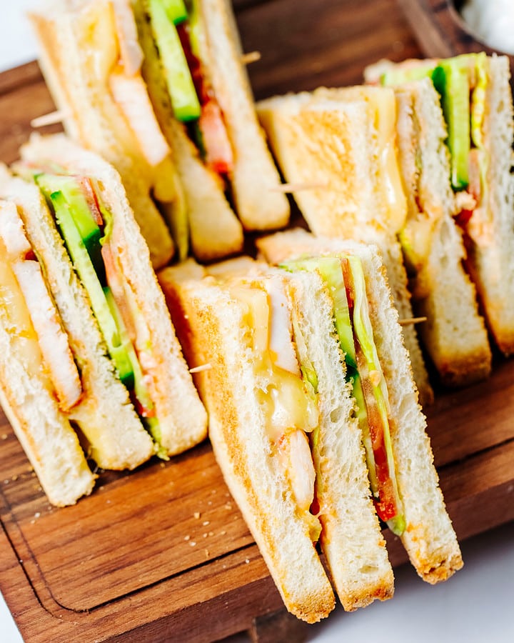 Close look of finger sandwiches served on a wooden cutting board.