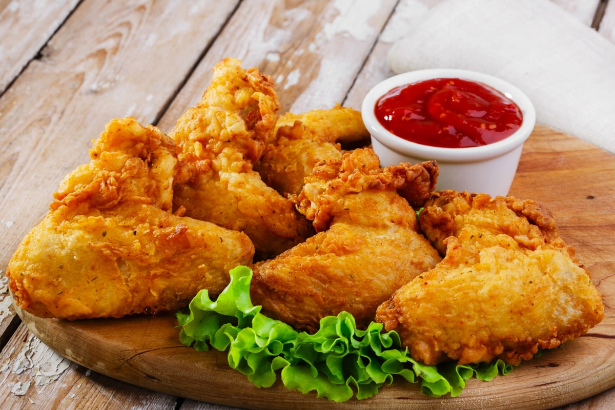 Close look of fried chicken legs on a wooden serving board and served with ketchup.