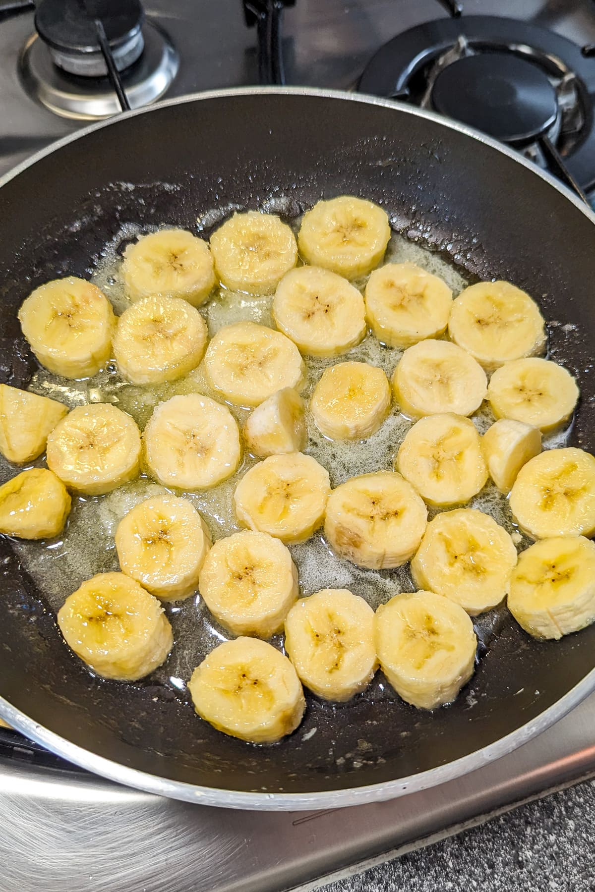 Caramelizing sliced bananas in melted sugar in a frying pan.