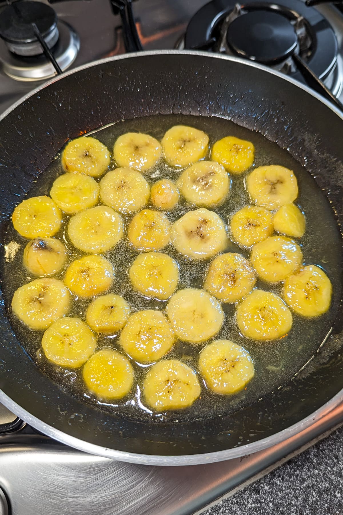 Caramelizing banana slices in a frying pan with melted sugar.