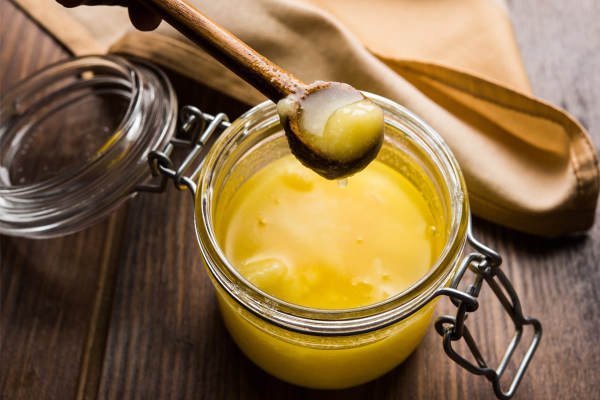 Wooden spoon over a transparent jar with clarified butter.