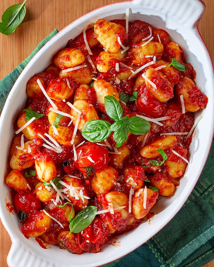 Top view of a casserole with gnocchi cooked in a tomato sauce and topped with parmesan and basil leaves.