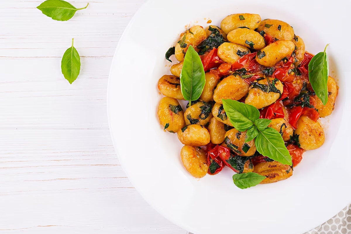 Top view of gnocchi cooked with roasted tomatoes and a few fresh basil leaves.