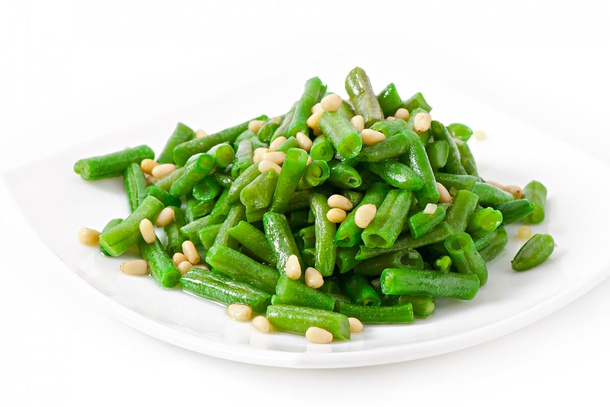 White plate with cooked green beans isolated on a white background.