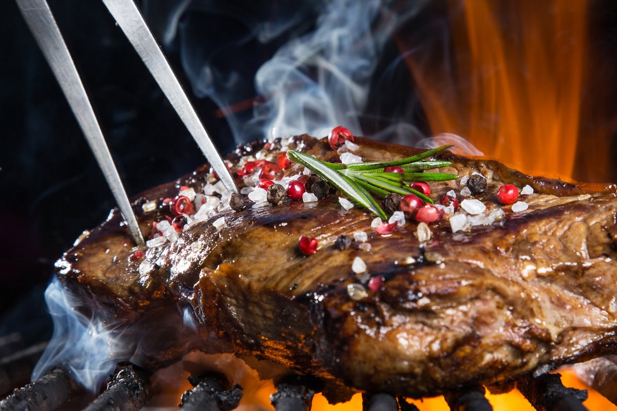 Close look of a charcoal steak with fire and smoke in the background.†
