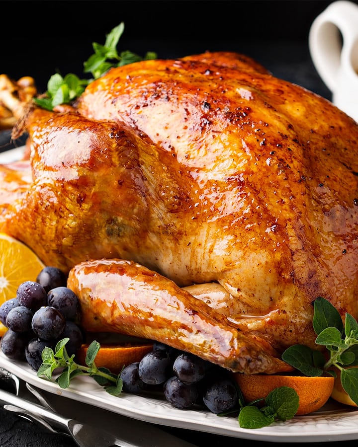 Close look of roasted turkey with grapes, and oranges.