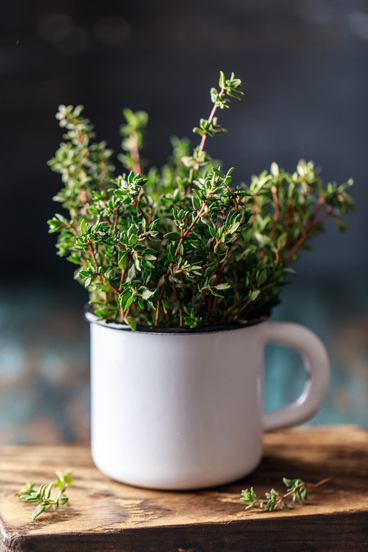 Close look of fresh thyme in a metal cup sitting on a wooden board.