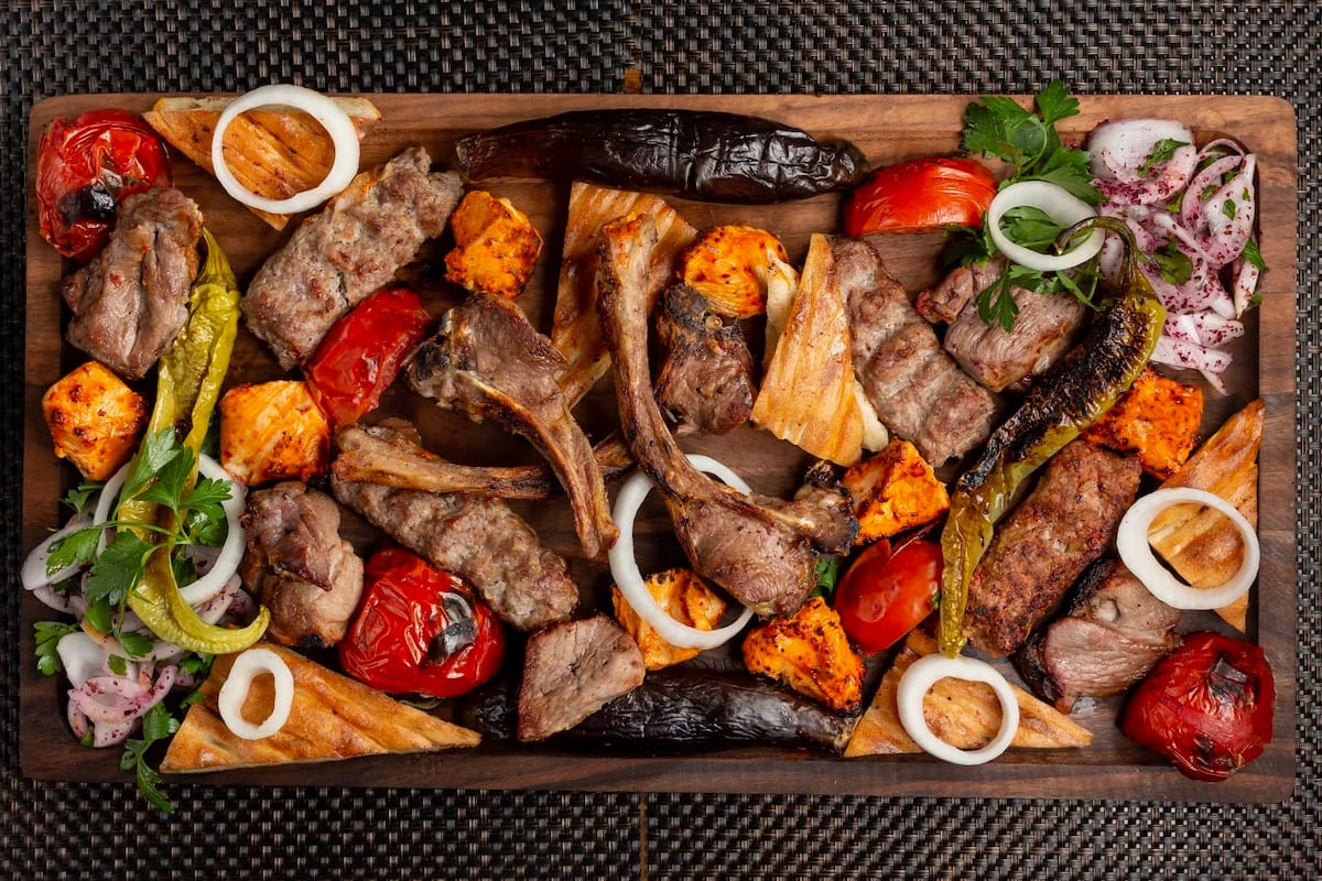 Top view of a wooden board with lamb, and different roasted vegetables.