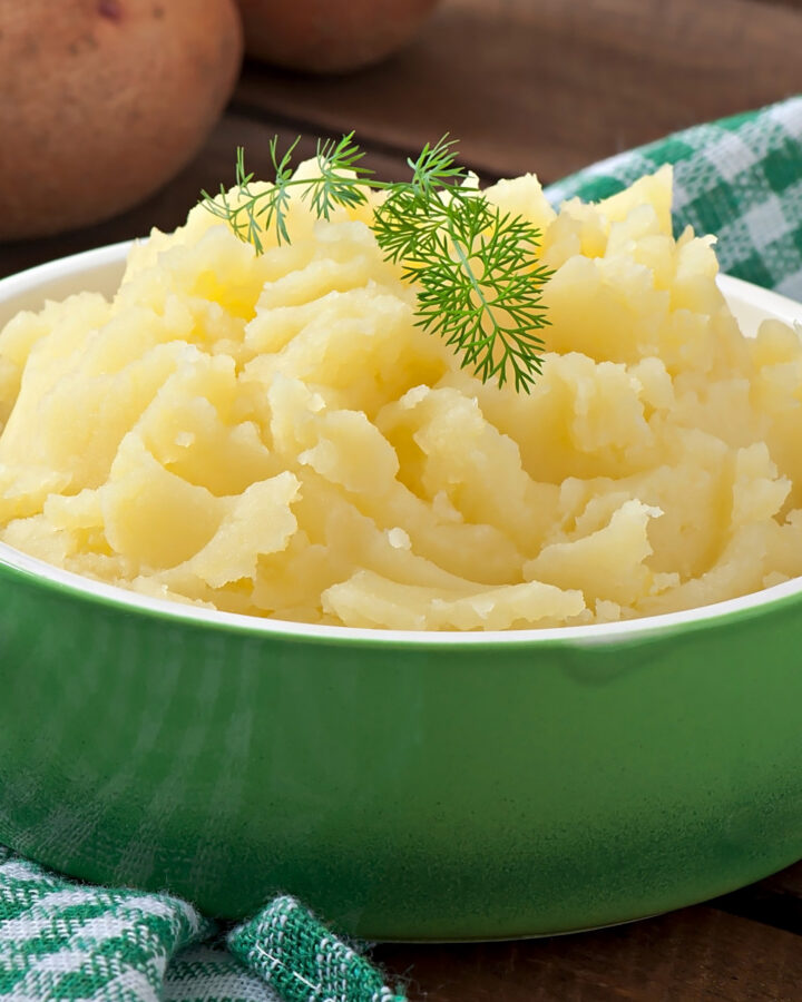 Close look of green bowl with mashed potatoes and topped with dill.