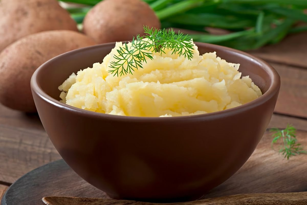 Close look of brown bowl with mashed potatoes and topped with dill.
