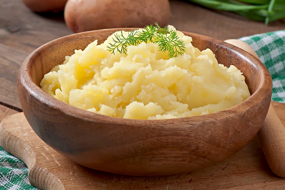 Close look of a wooden bowl with mashed potatoes and topped with dill.