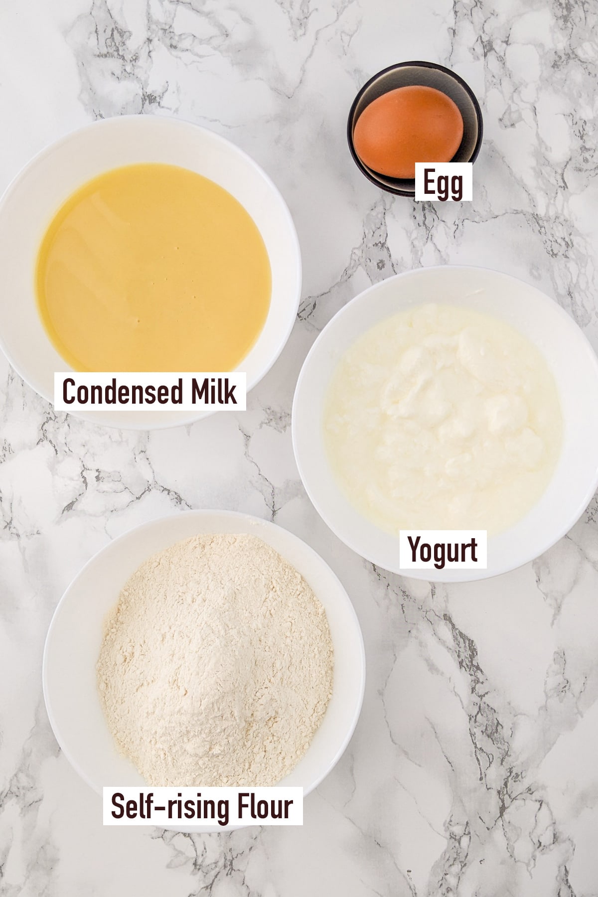 Top view of yogurt, self-rising flour, condensed milk and an egg.