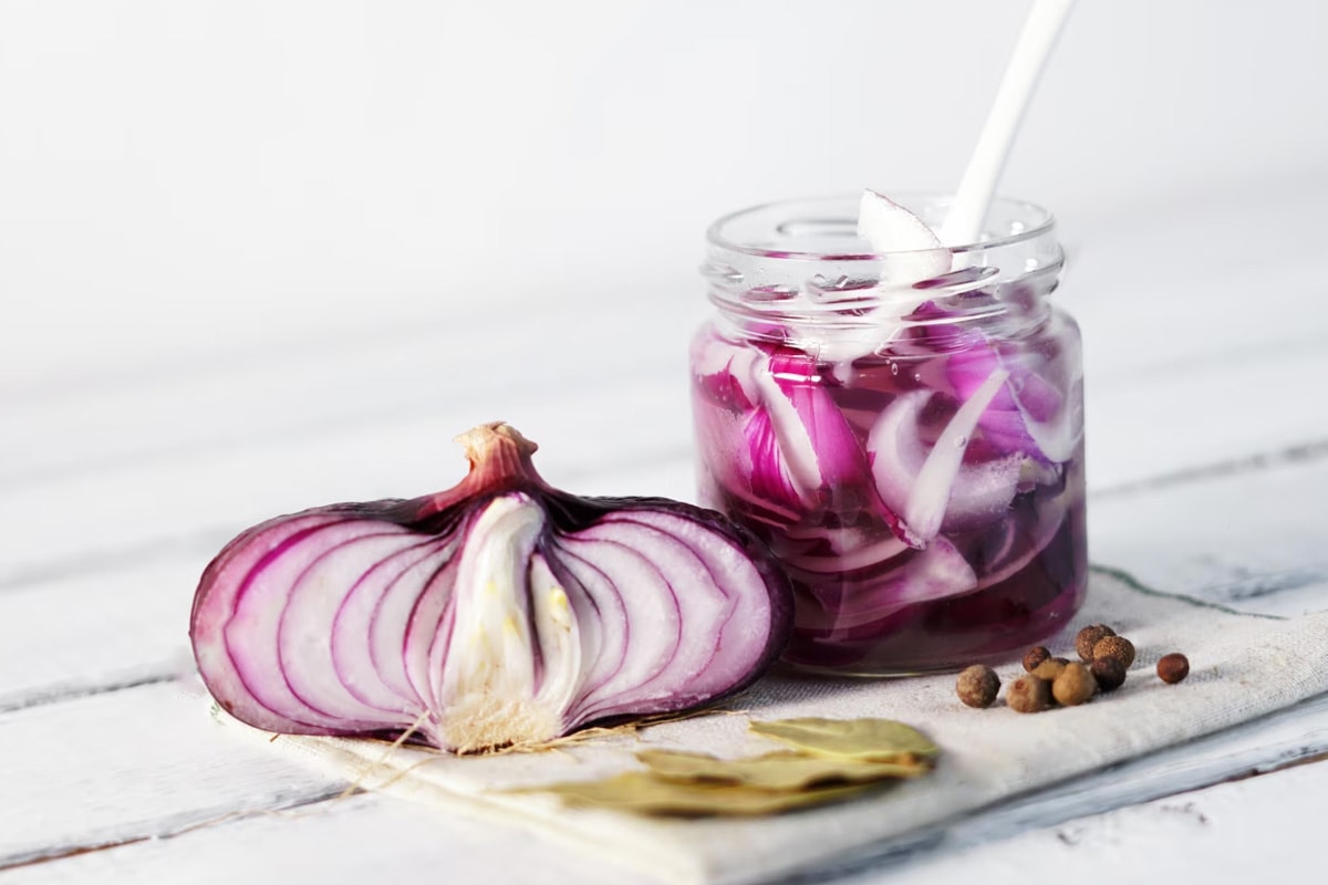 Close look of a transparent jar with pickled onions on a white wooden table.