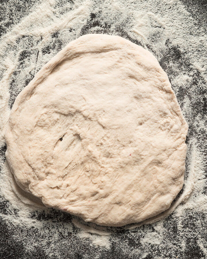 Pizza dough on a black table full with all-purpose flour.