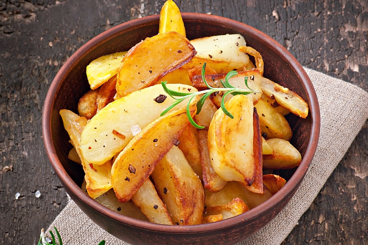 A brown vintage plate full with roasted potato wedges.