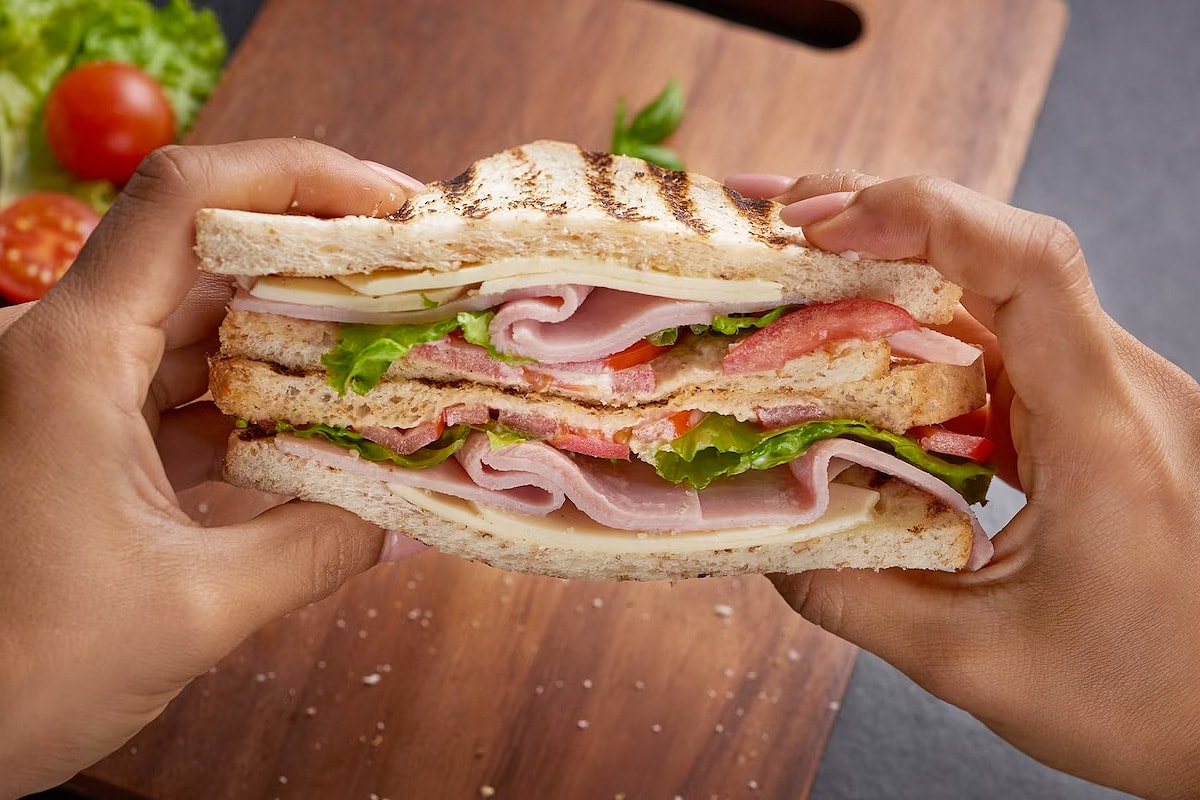 Two woman's hands holding a large sandwich.