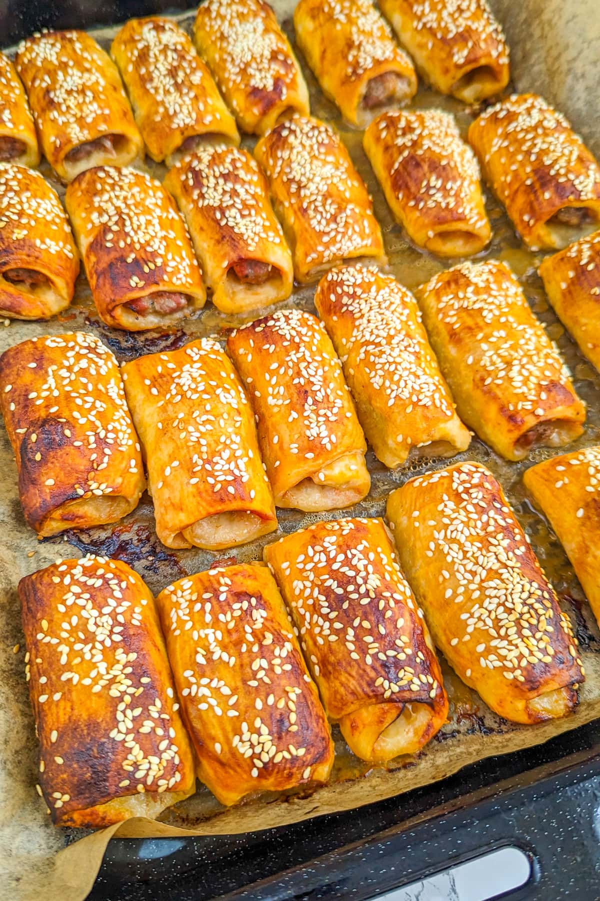 Close look of a tray bake with sesame sausage rolls.