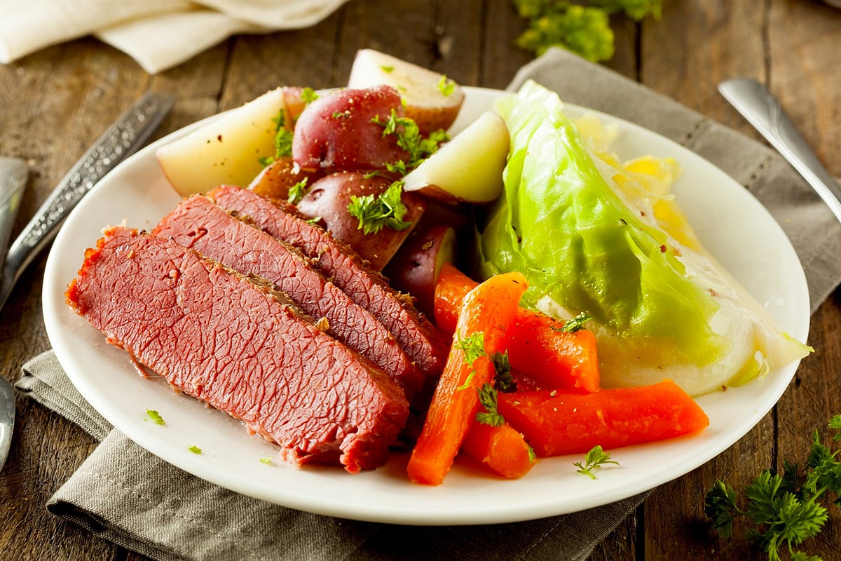 Close view of corned beef near some cooked vegetables.