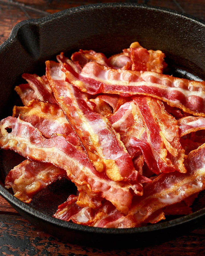 Close view of an iron skillet with fried bacon slices.