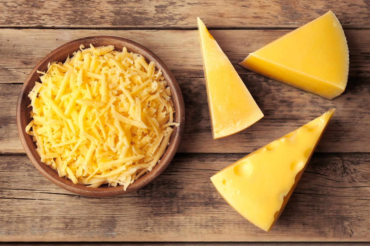 Top view of 3 pieces of cheddar near a plate with shredded cheddar cheese.