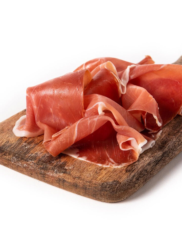 Wooden cutting board with sliced ham isolated on a white background.