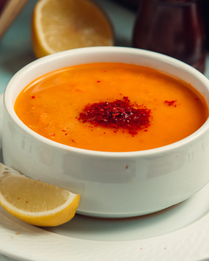Orange creamy soup served in a white soup bowl near a slice of lemon.