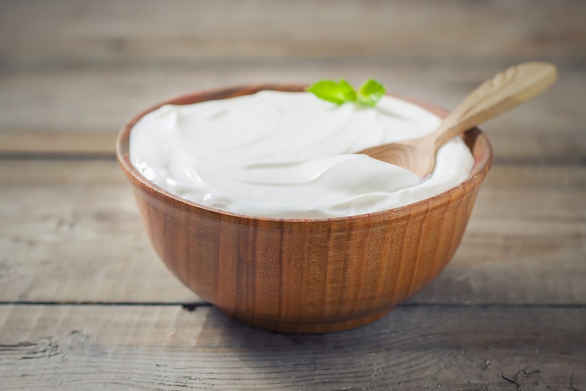 A wooden bowl with Greek yogurt and a wooden spoon.