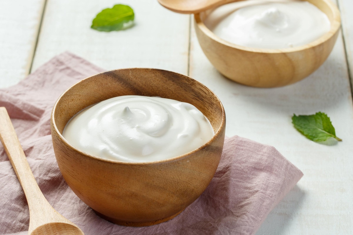 Two wooden bowls with Greek yogurt on a white wooden table.