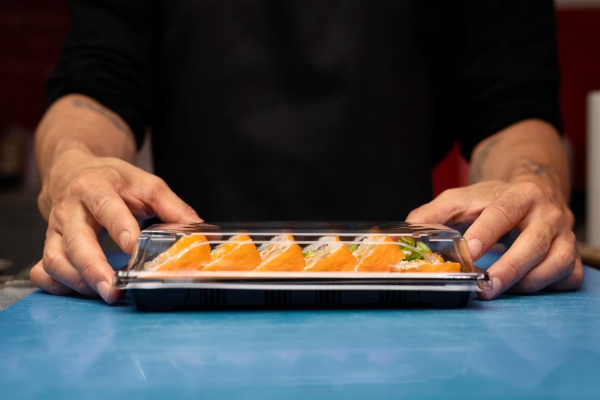 Man serving sushi rolls sealed in a transparent box.