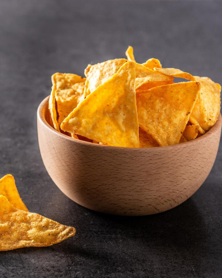 A wooden bowl with tortilla chips on a dark gray background.