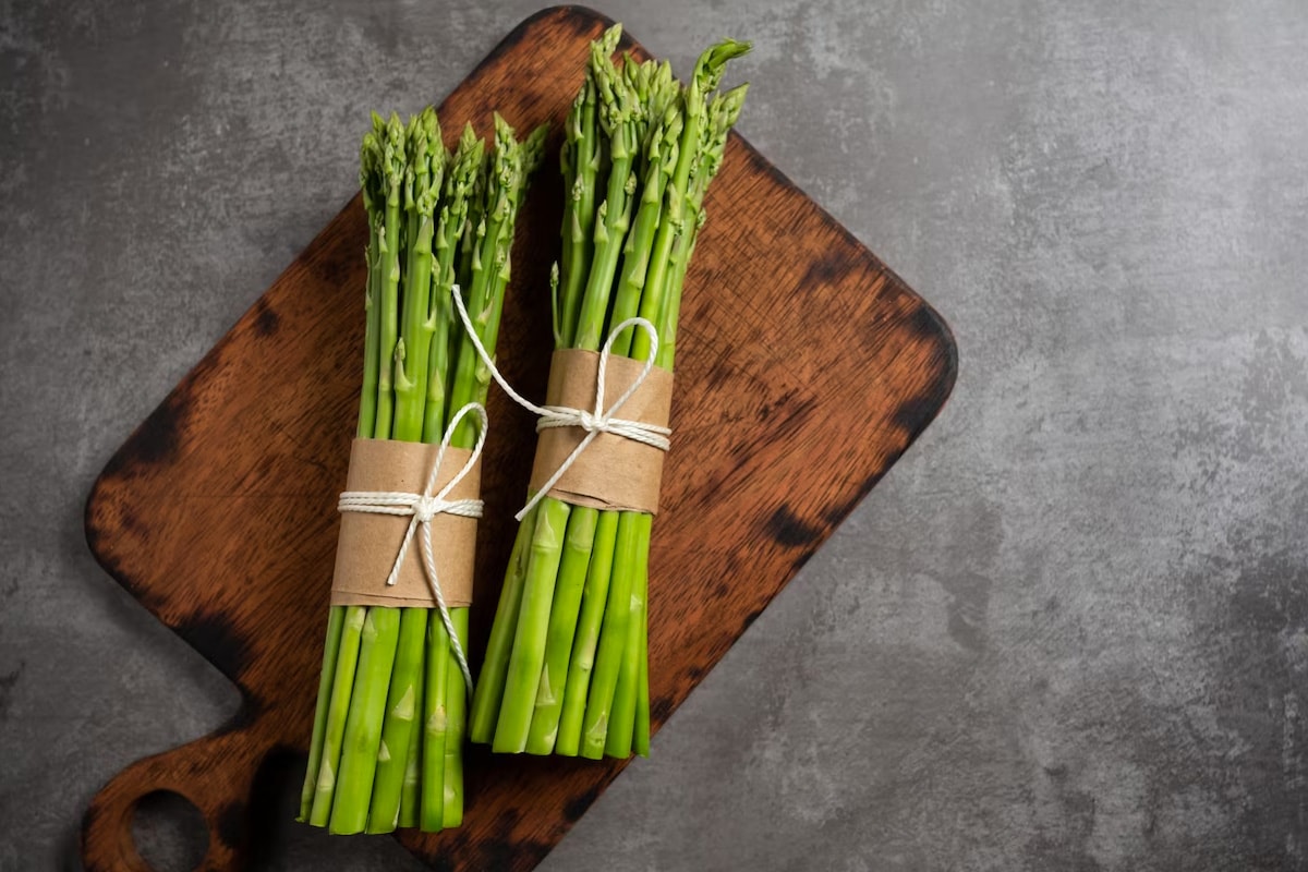 Top view of two heaps of fresh asparagus on a wooden cutting board.