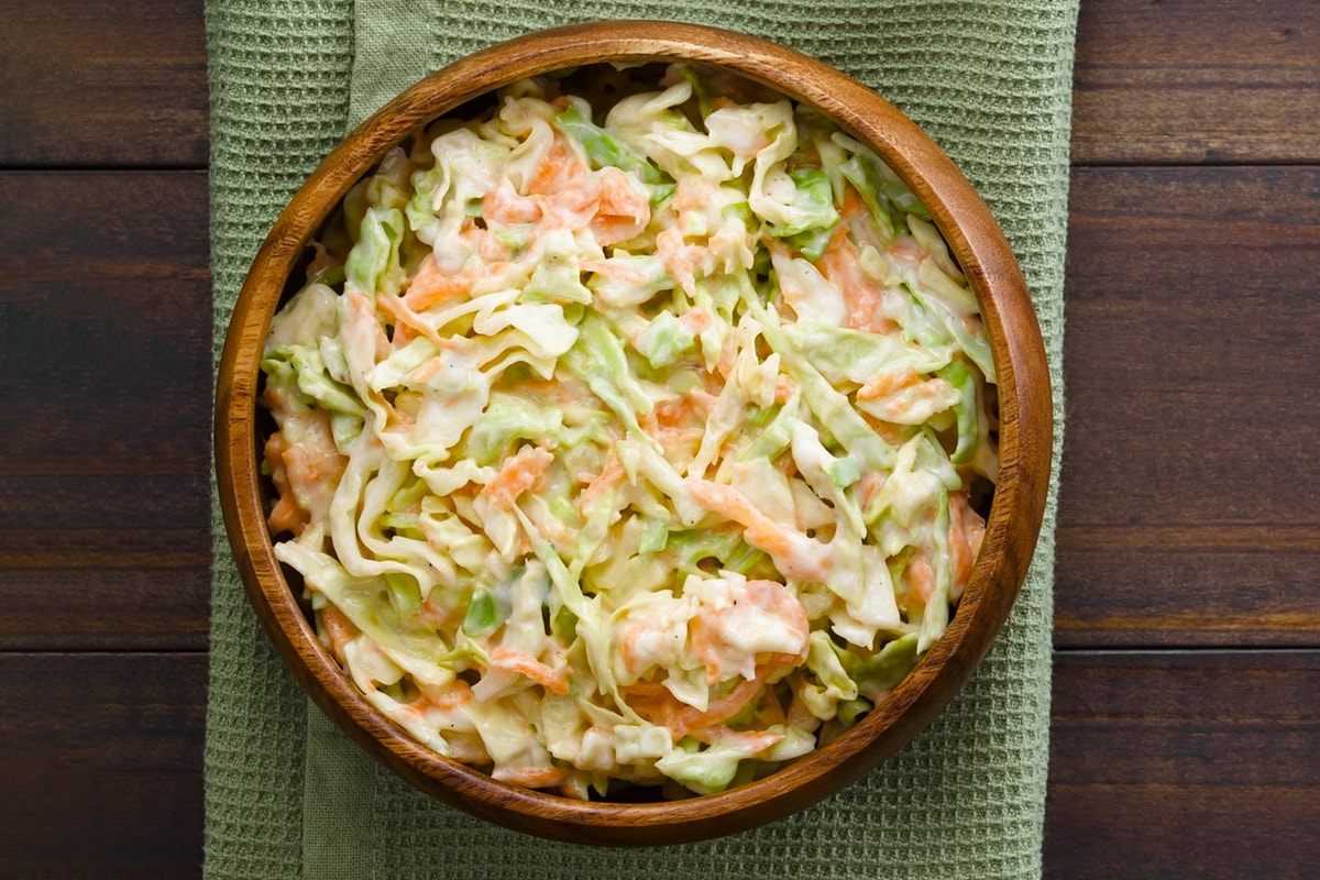 Top view of a wooden plate with coleslaw salad in it.