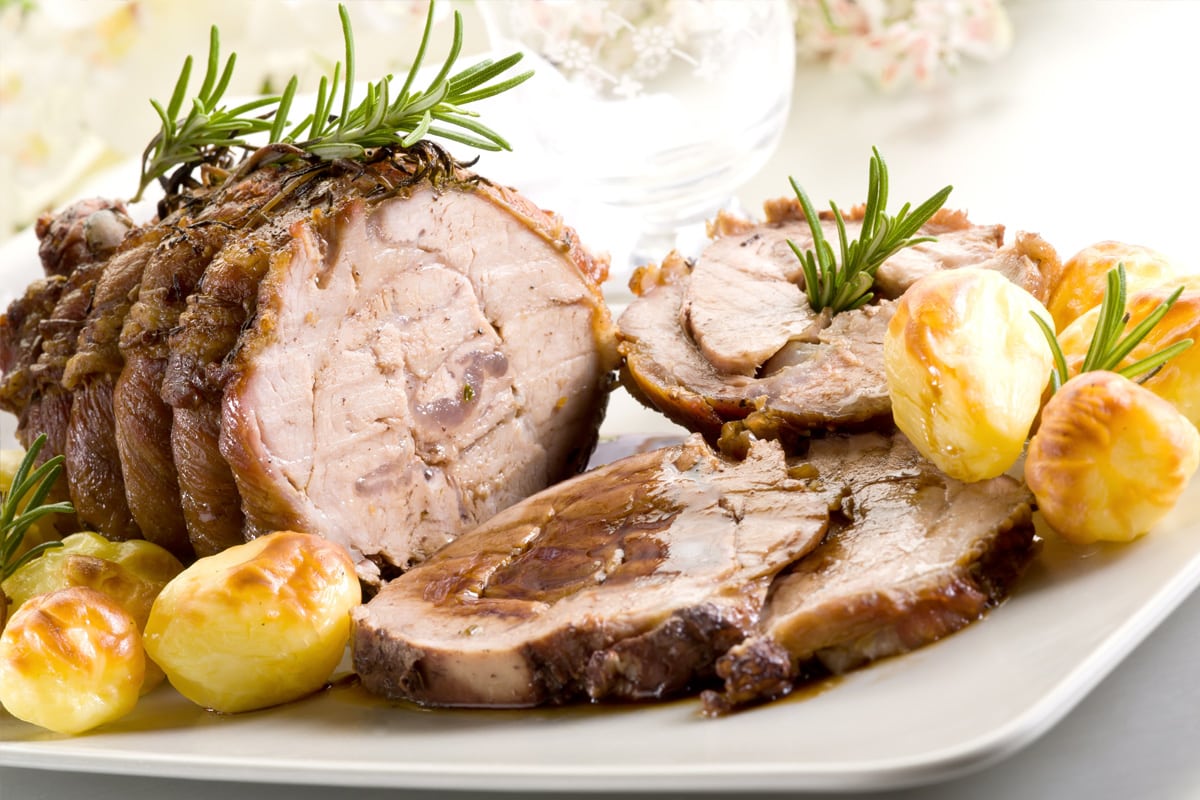 Close look of cooked roast with sauce, rosemary and baked potatoes.