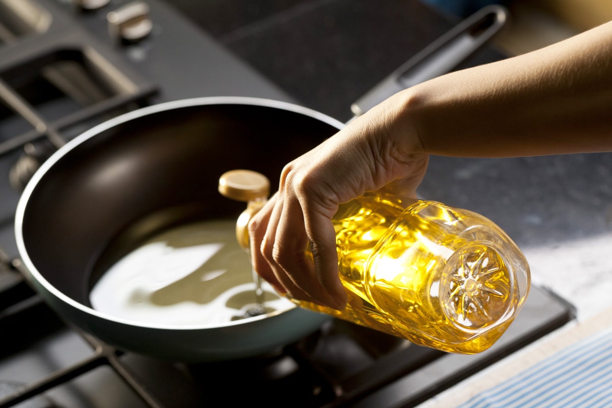A woman hand pouring oil into a frying pan.