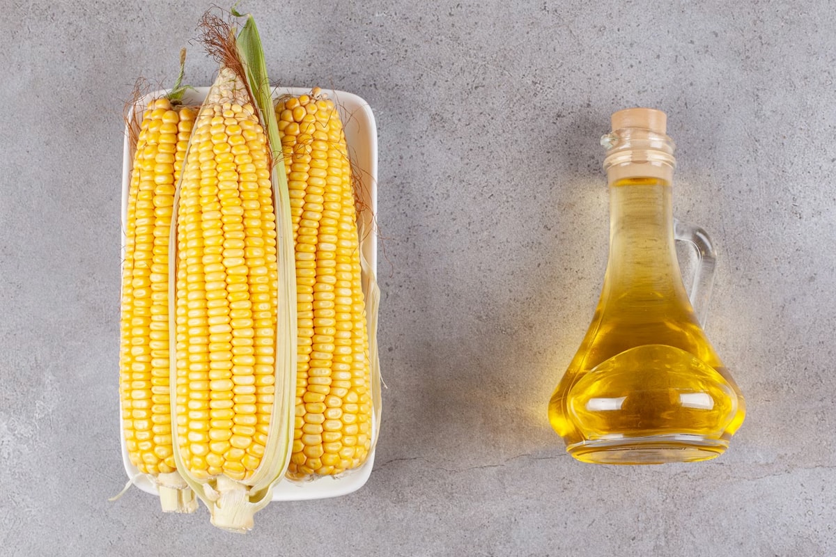 Top view of 3 raw corns near a bottle with corn oil.
